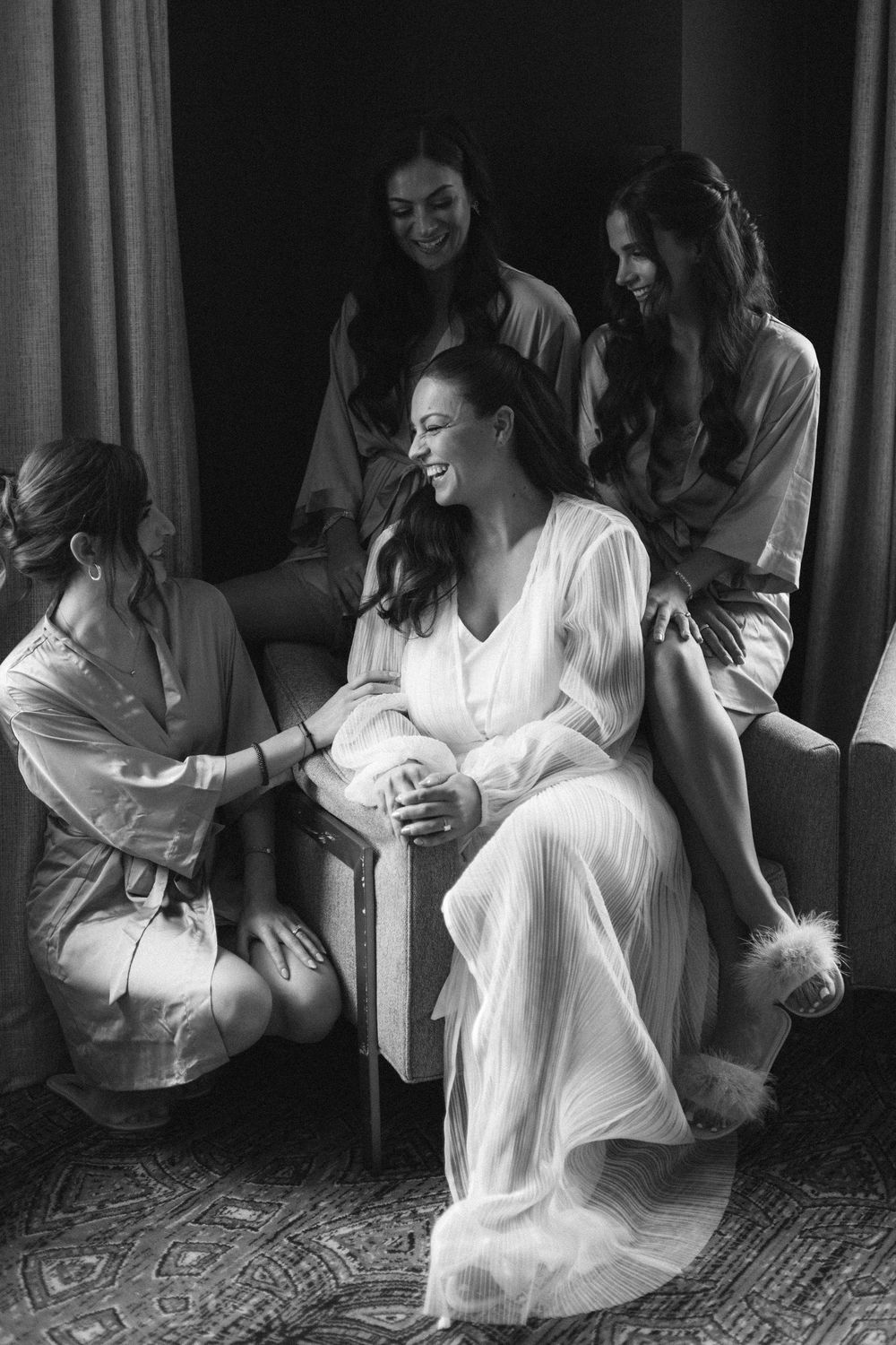 Black and white photo showing bride and bridesmaids in a joyful moment getting ready together before wedding in a Chicago bridal suite.