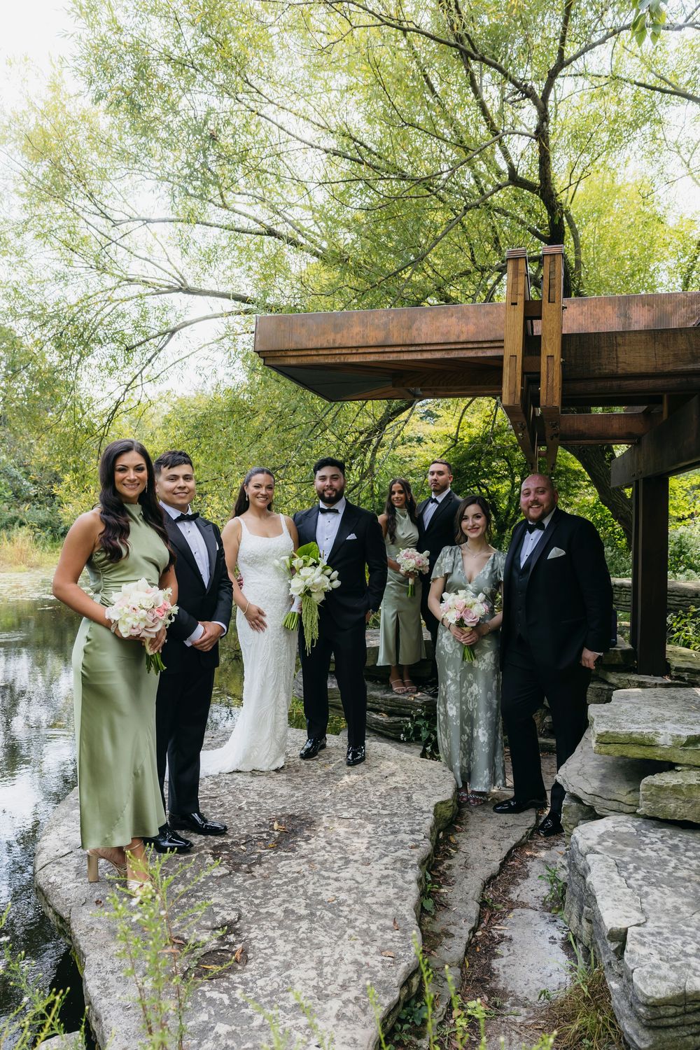 Wedding party stands together on stone path under wooden pergola in Chicago Alfred Caldwell Lily Pool.