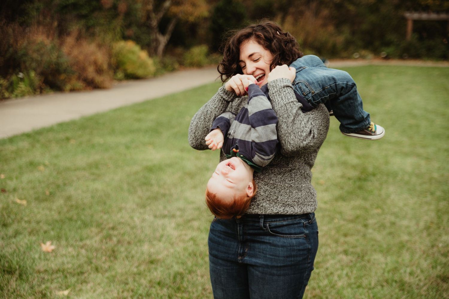 A playful moment outdoors with a child being lifted up while wearing a striped sweater on a fall day.