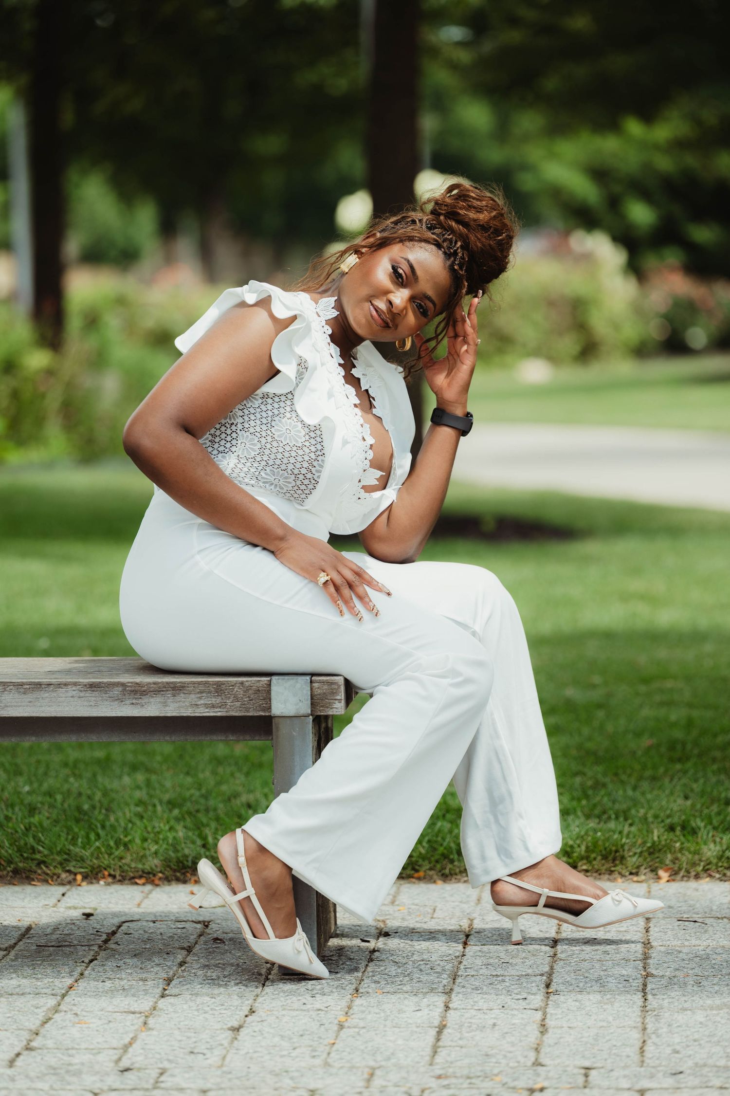 A person in a white lace jumpsuit poses gracefully on stone steps in a lush garden setting.