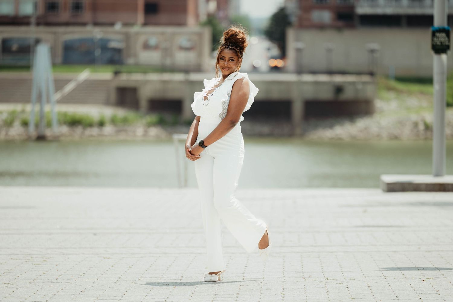 A person in a white dress twirls gracefully in an urban plaza on a sunny day.