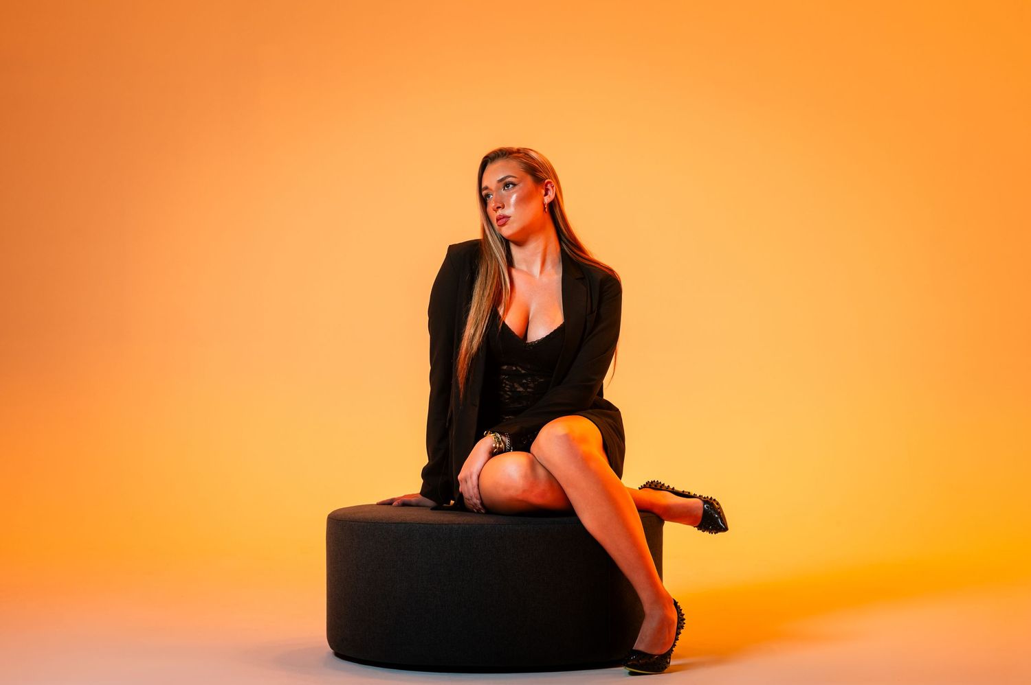 Woman in black outfit poses against vibrant orange background in artistic photo series.