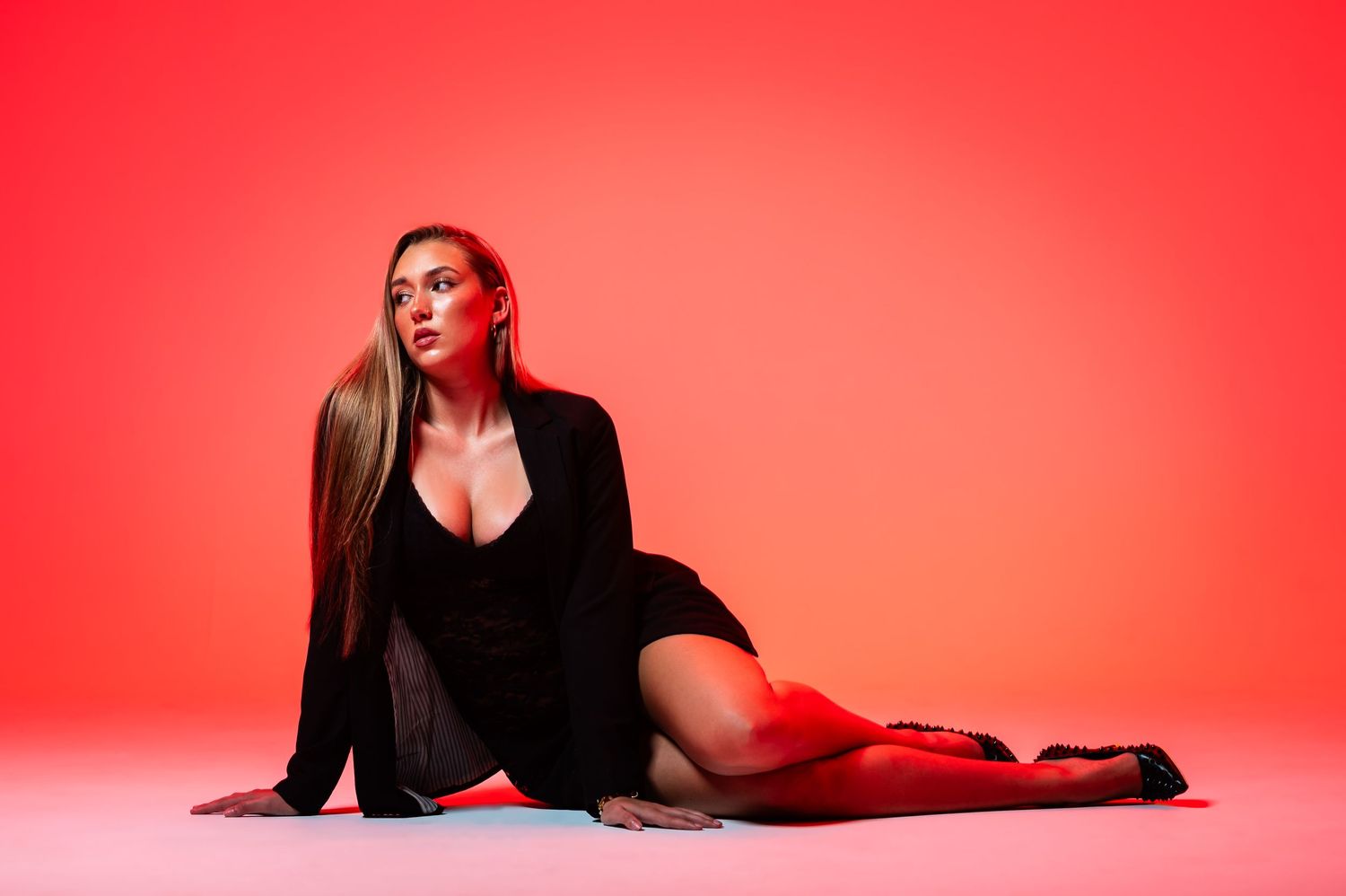 A person in black clothing poses gracefully against a vibrant red studio backdrop.