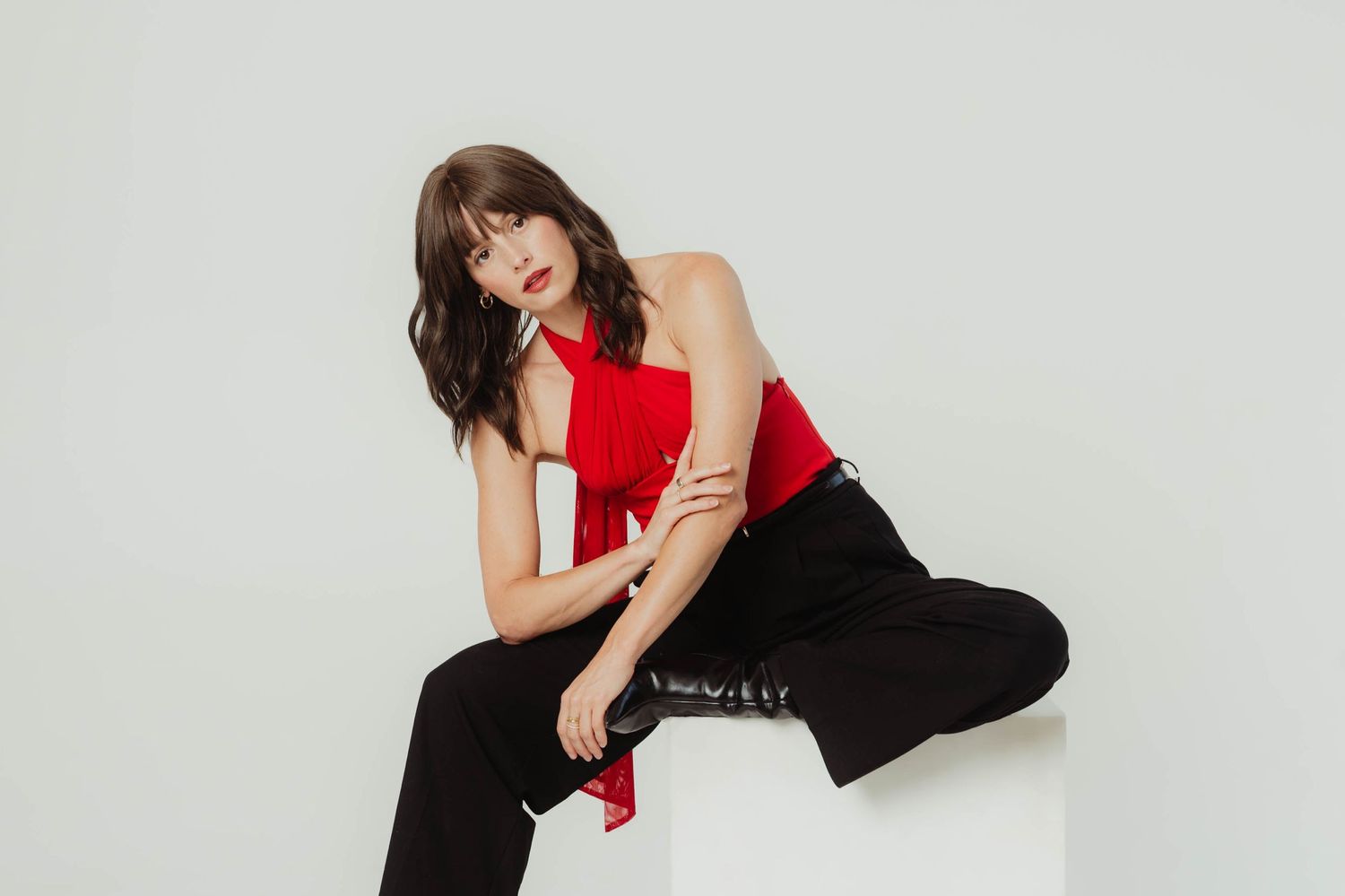 Dancer in red top and black pants performs expressive contemporary dance movements against white background.