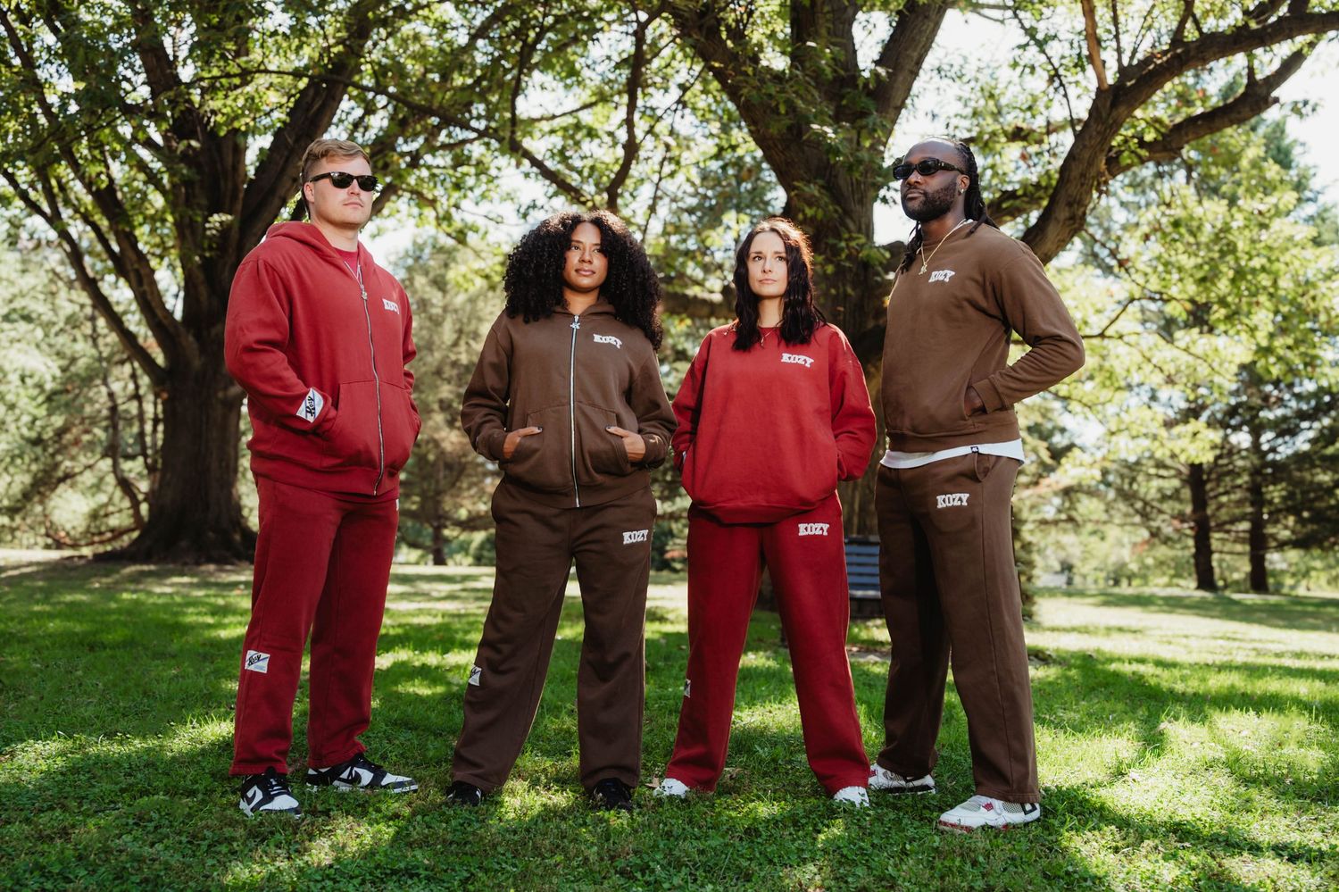 A group of people in red and brown clothing stand together on grass under trees during a casual outdoor gathering.