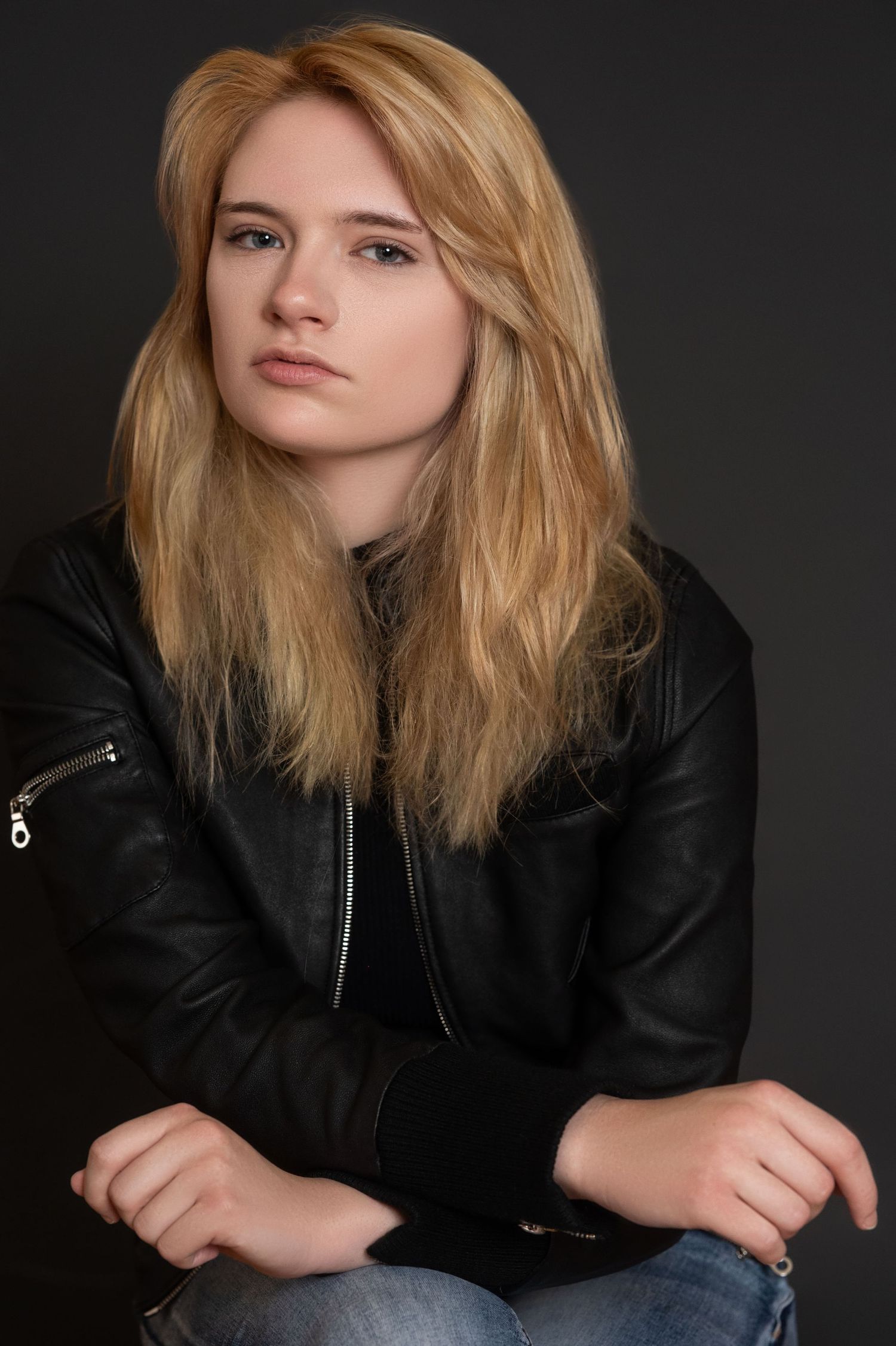 Portrait against dark background showing blonde hair and black leather jacket in moody studio lighting.