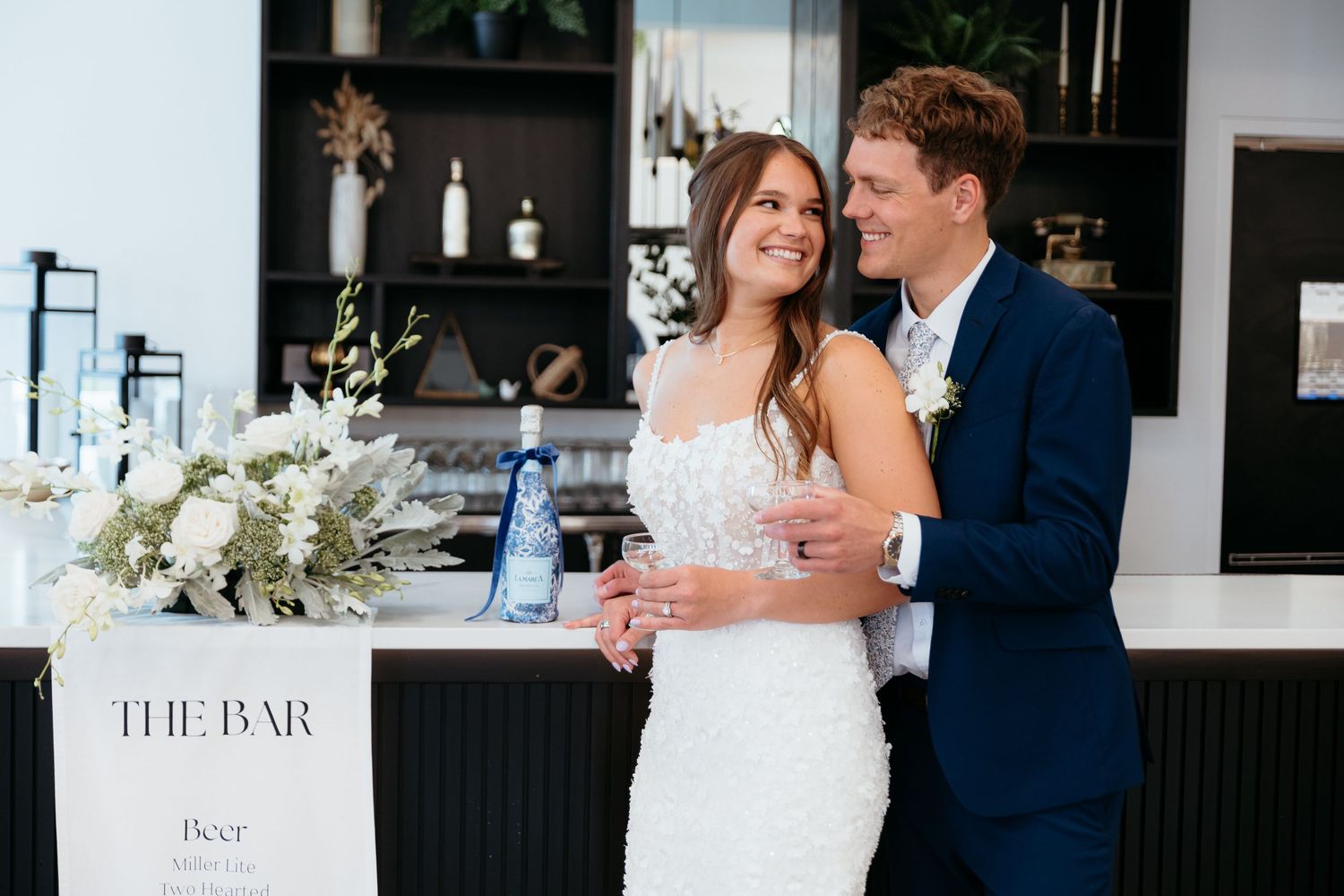Wedding couple dancing together in modern venue with bar signage in background.