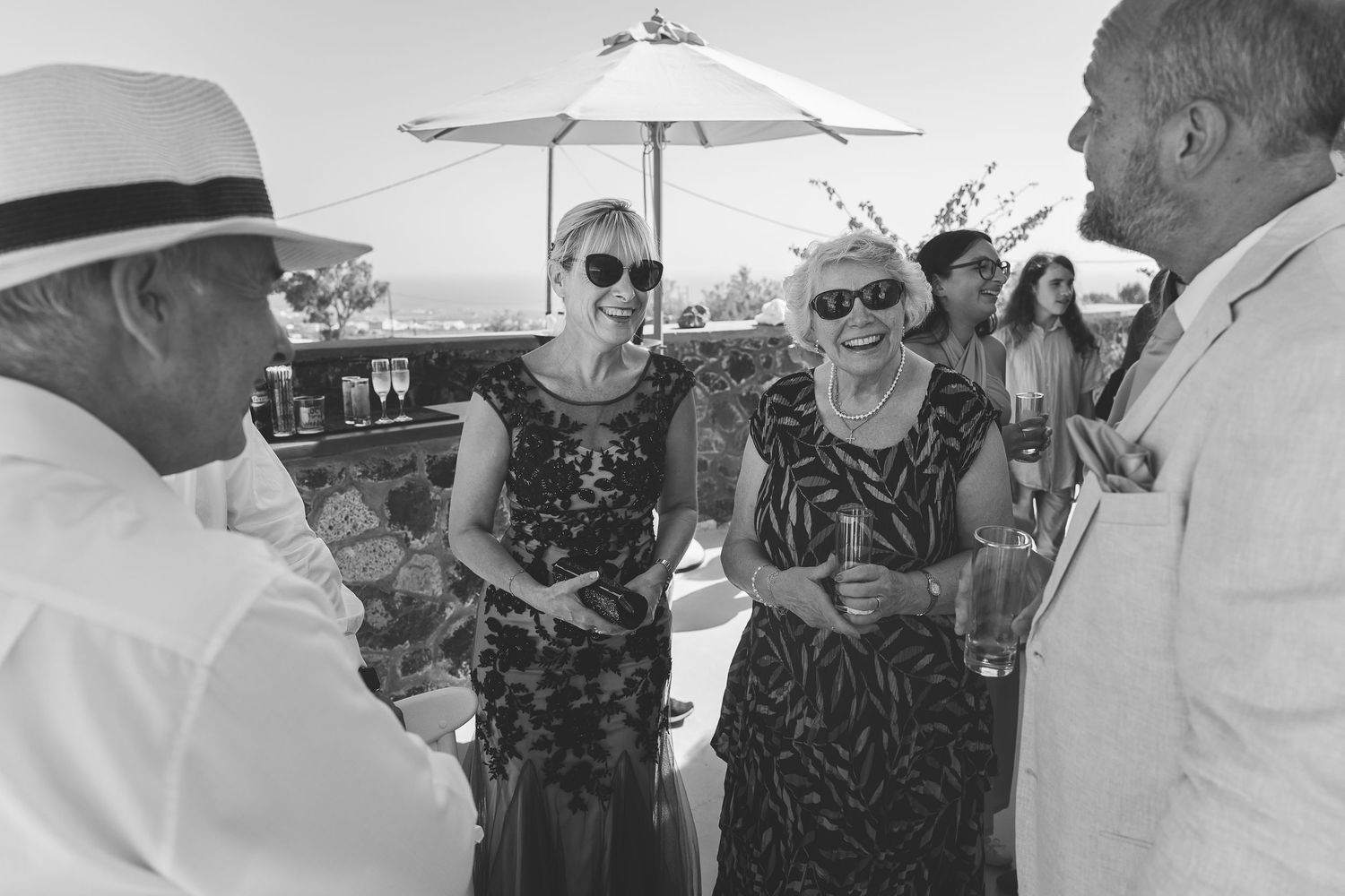 A black and white photo of wedding guests in Santorini having a cheerful conversation.