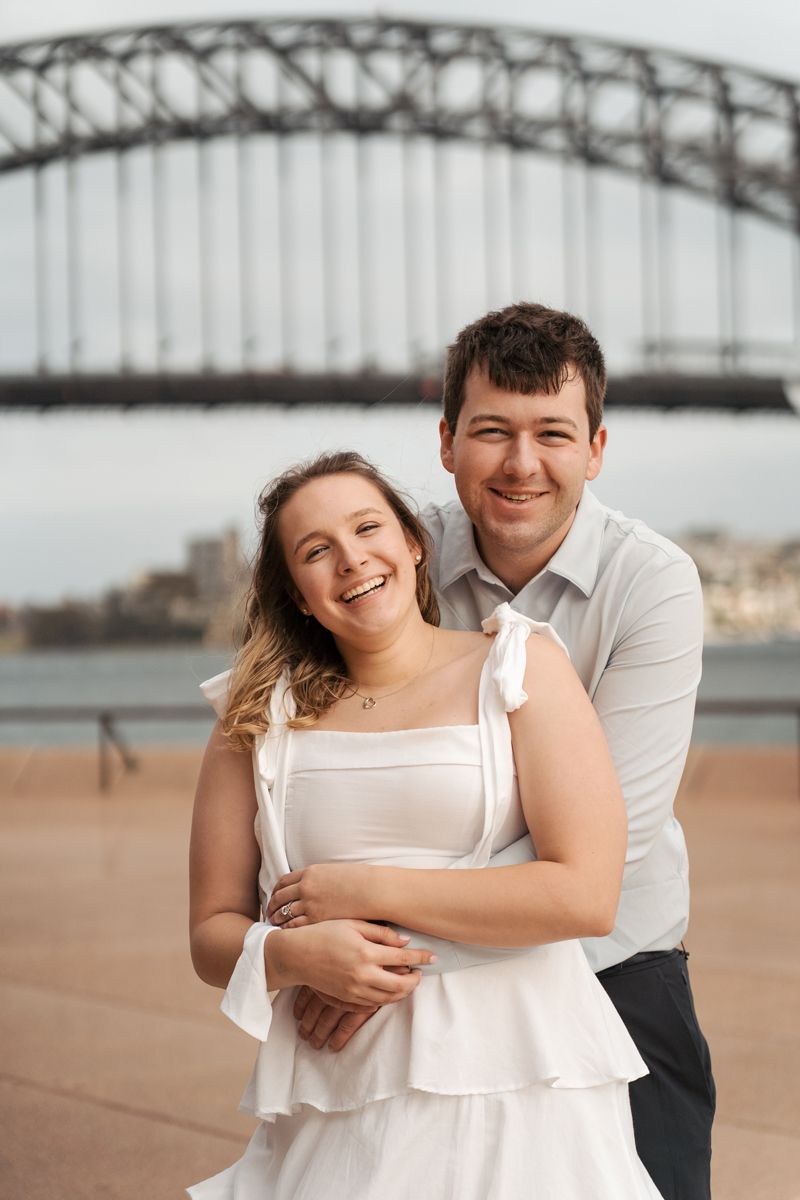 A romantic engagement photo session near a bridge showing a couple embracing and laughing together in sydney