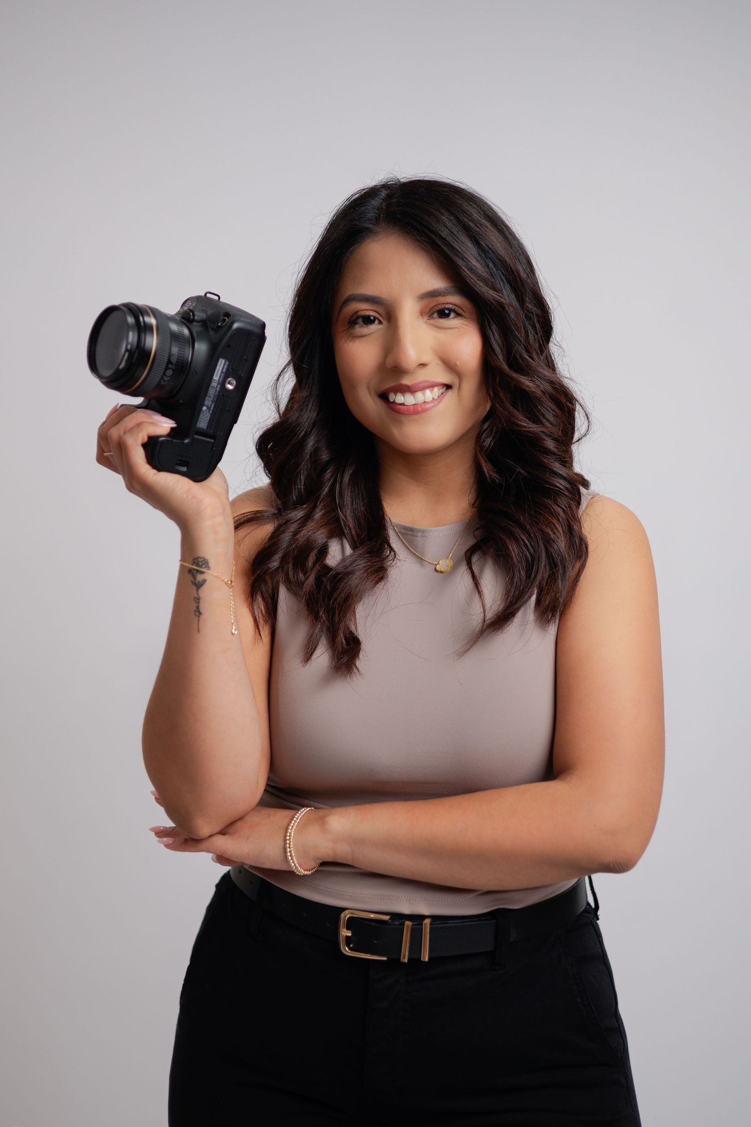 Female photographer smiling confidently while holding a DSLR camera in a professional studio portrait.