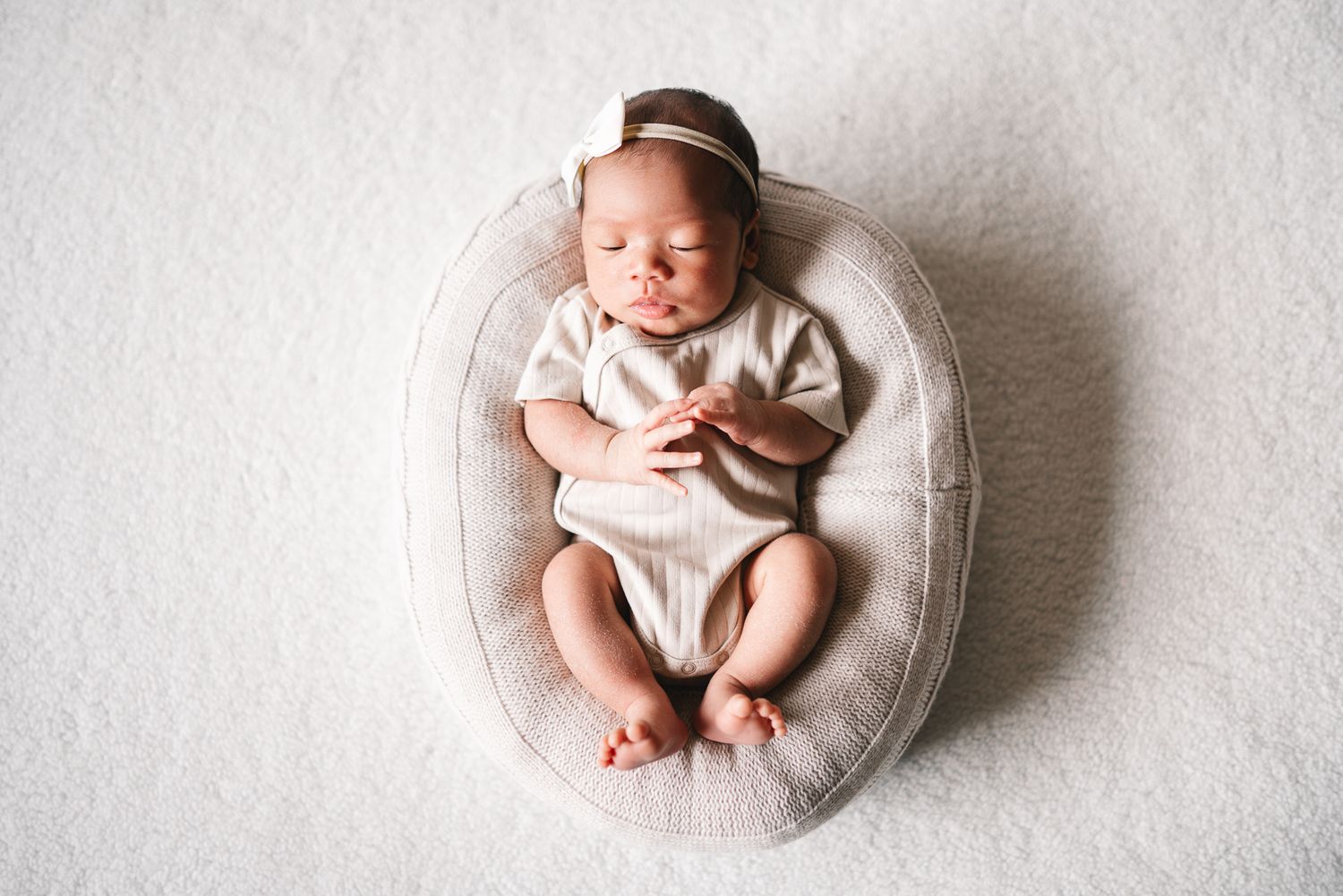 Newborn baby sleeping peacefully in cream-colored outfit on round cushion against white background taken by Melbourne newborn photographer.