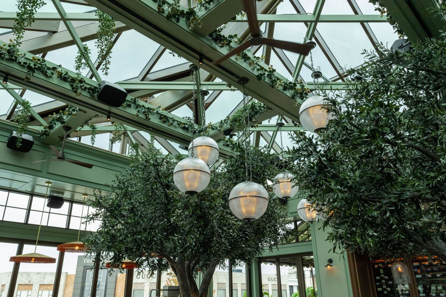 An elegant indoor atrium with lush green trees, globe pendant lights, and a glass ceiling.