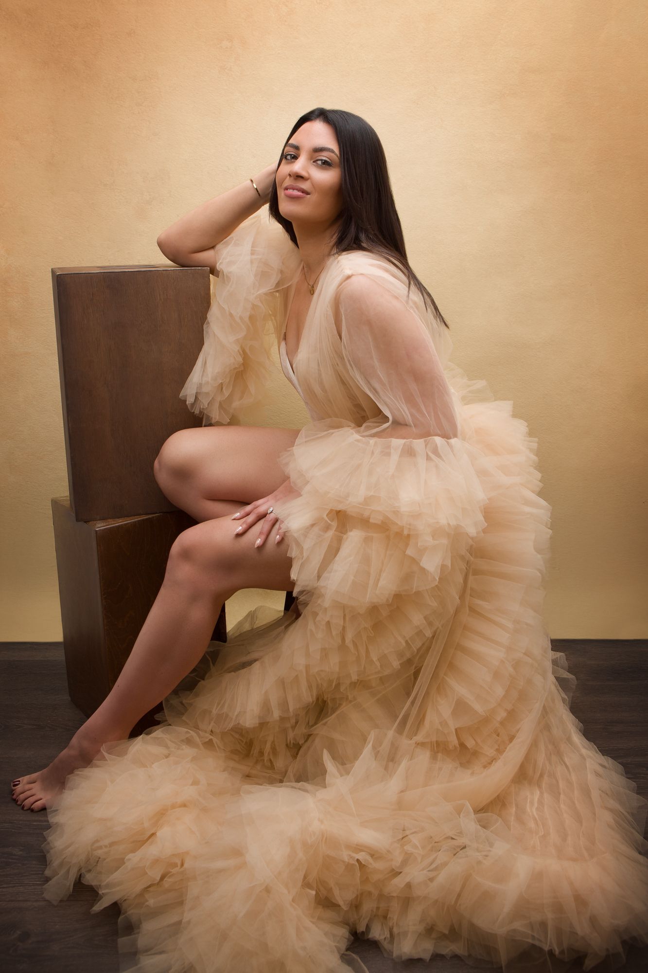 Ethereal boudoir portrait featuring a flowing champagne-colored tulle gown against a warm beige backdrop.