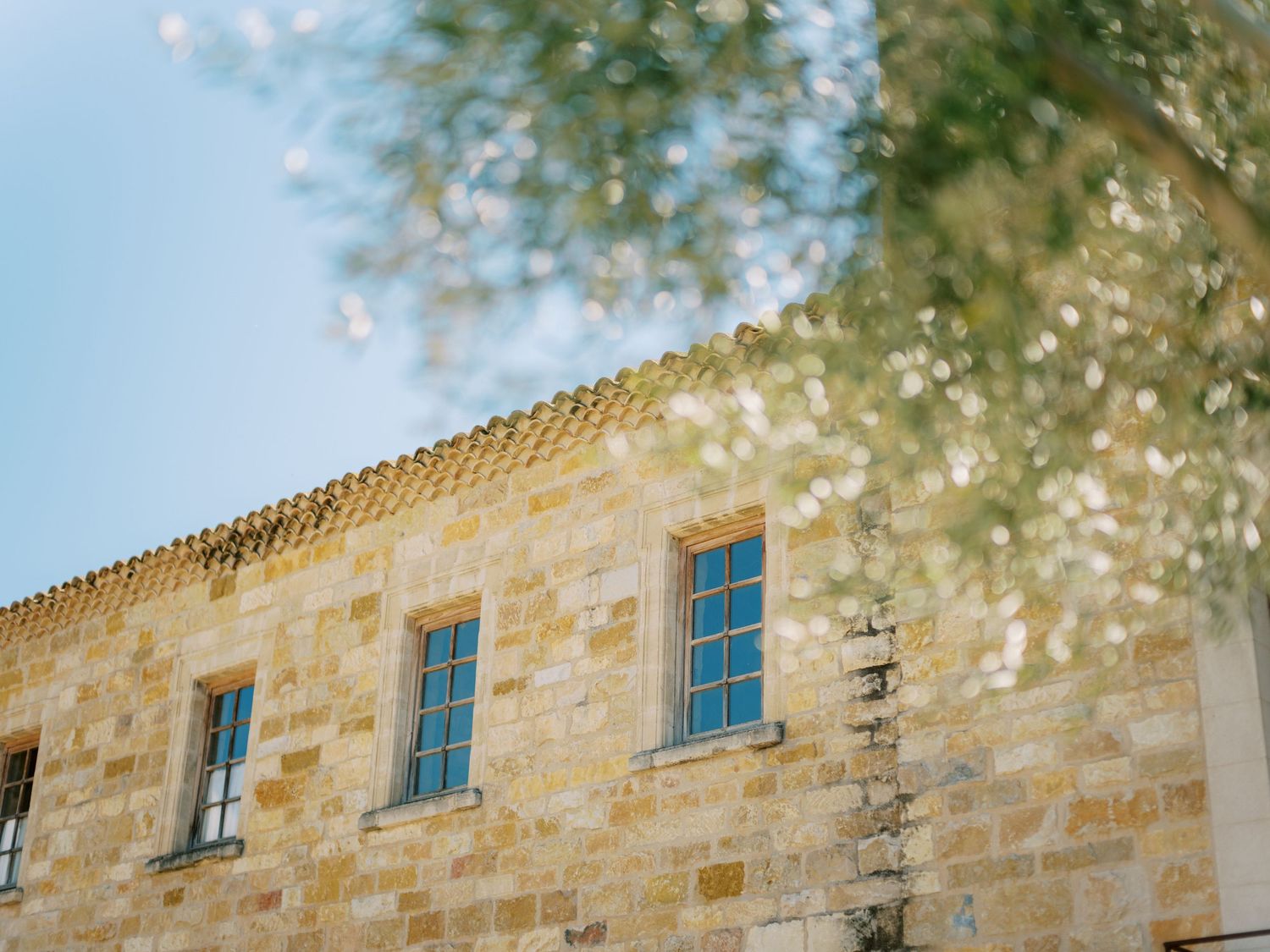 Sandstone building exterior with three blue windows against a bright sky.