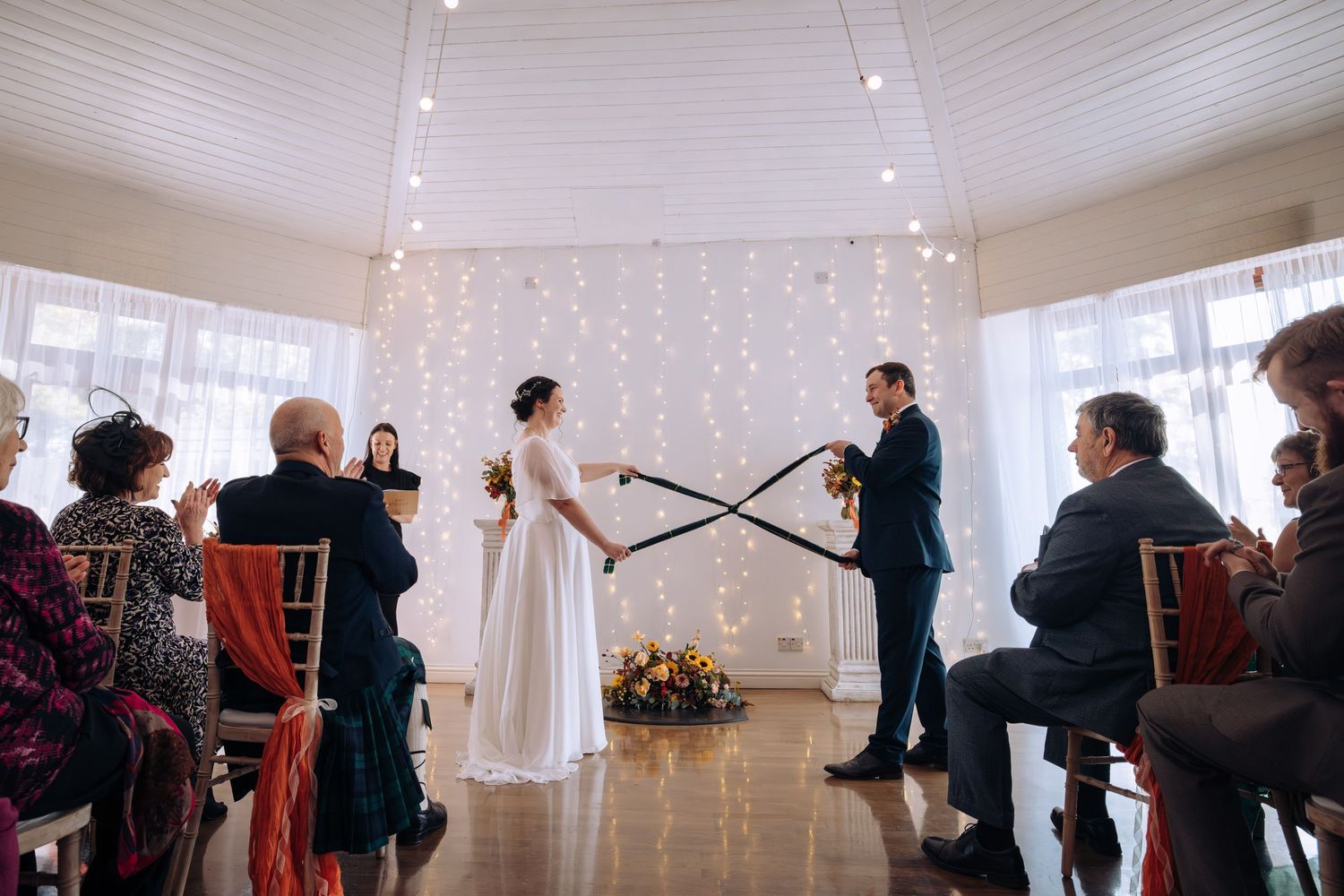 Wedding guests gather under white twinkle lights in an elegant reception venue during a celebration.