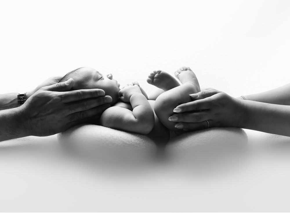 Black and white newborn photography detail of parents hands holding baby feet in Austin studio