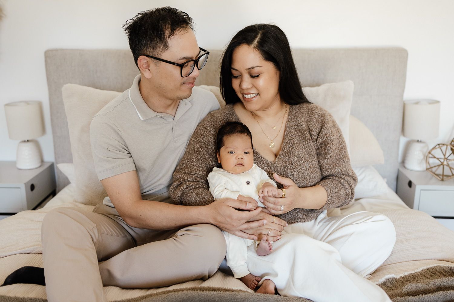 family sits on their bed with their baby at their in-home newborn photography session in San Jose