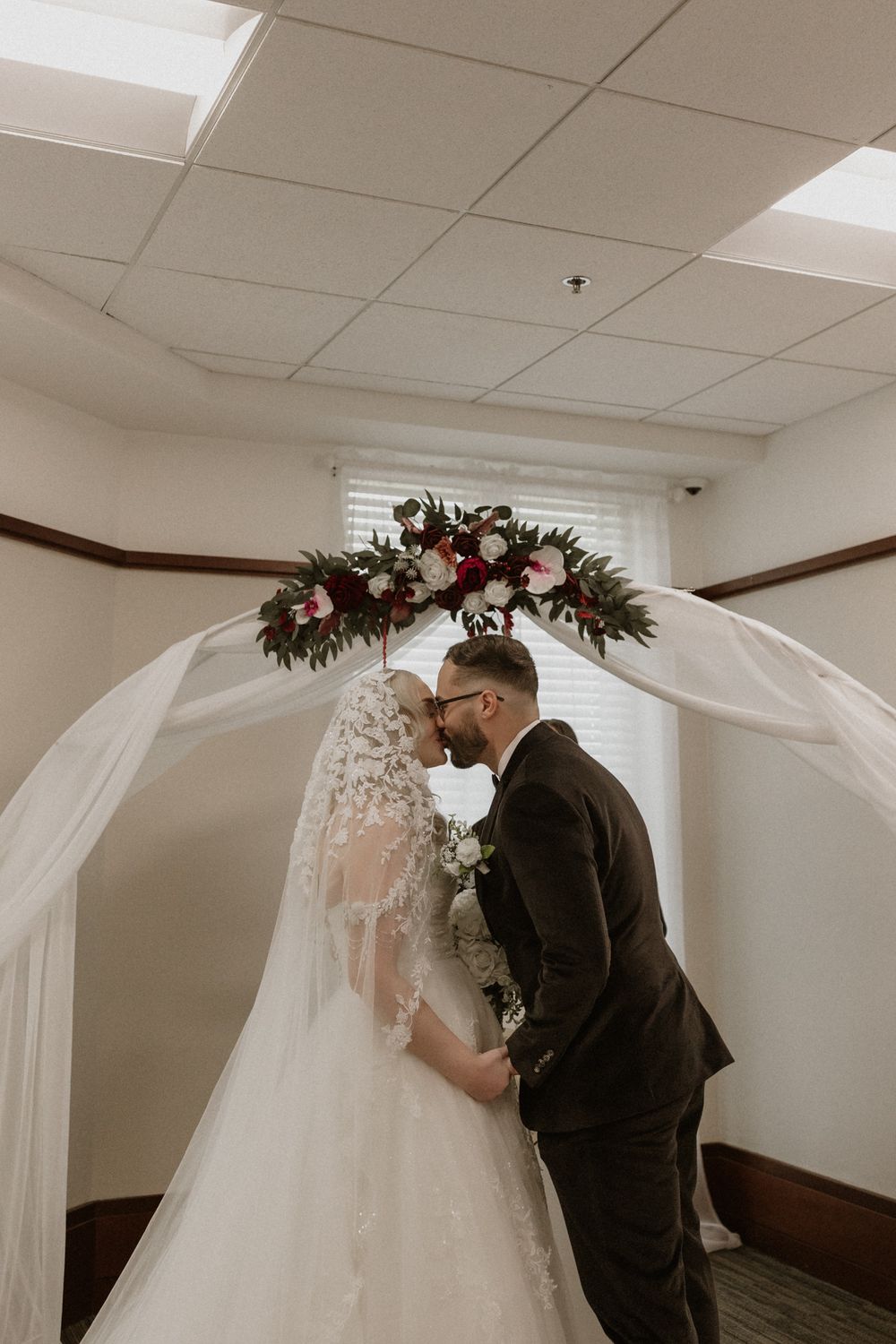 A romantic first look moment between newlyweds in an indoor venue decorated with white draping and floral arrangements.