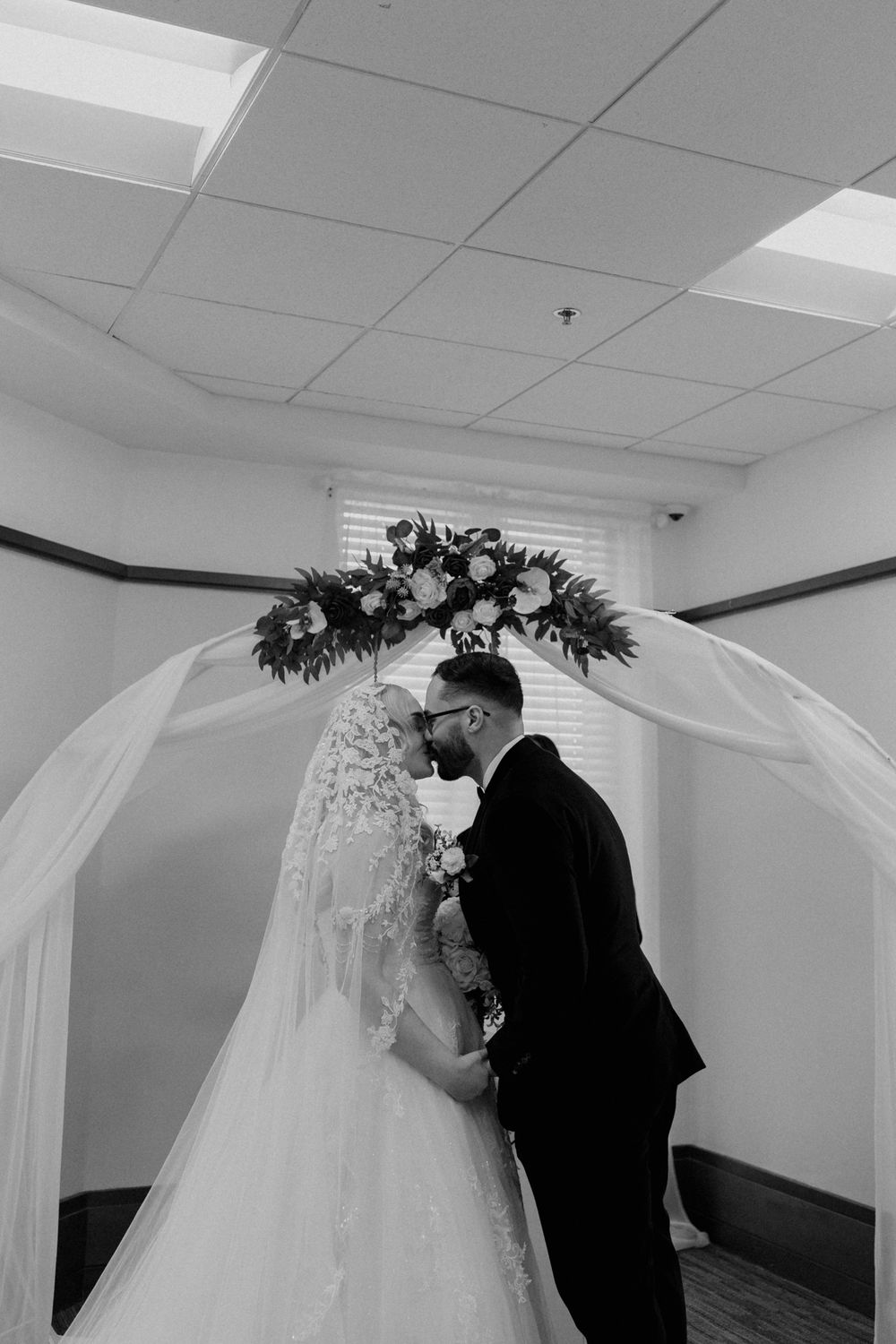 Bride and groom share an intimate moment under white drapery and floral decor during their wedding ceremony.
