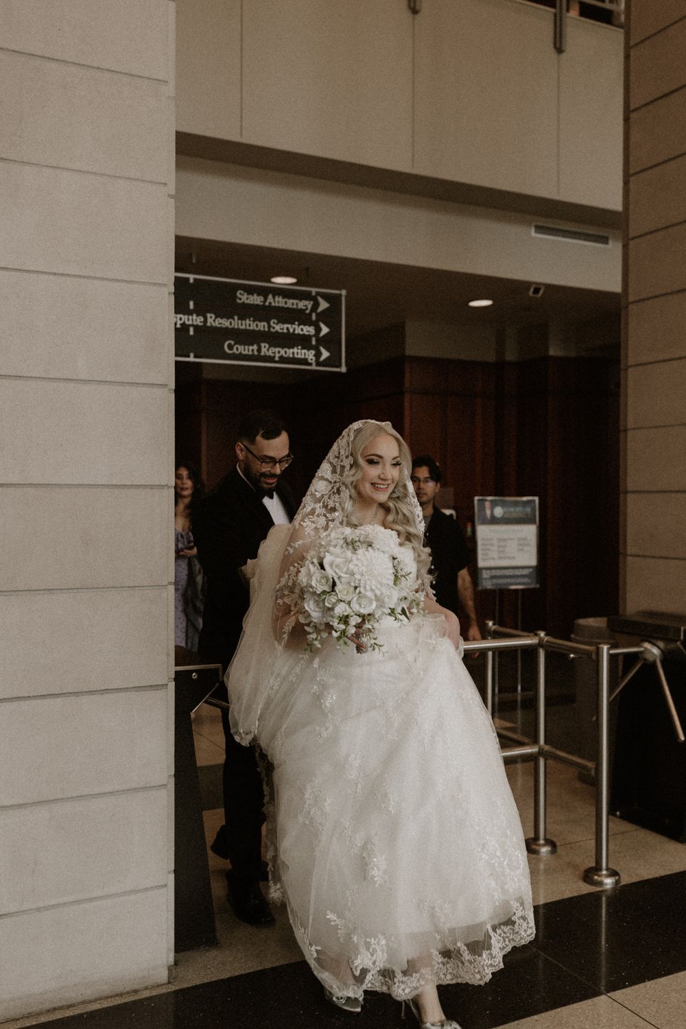 A bride in a white ballgown wedding dress enters through glass doors at a venue.