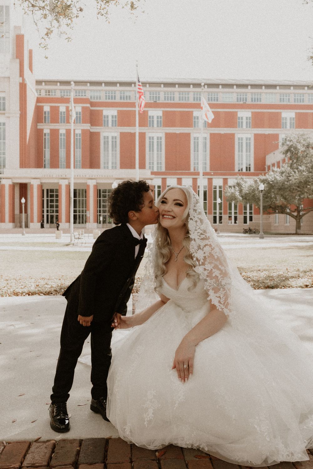 Wedding couple poses playfully for photos outside a grand brick building with white columns.