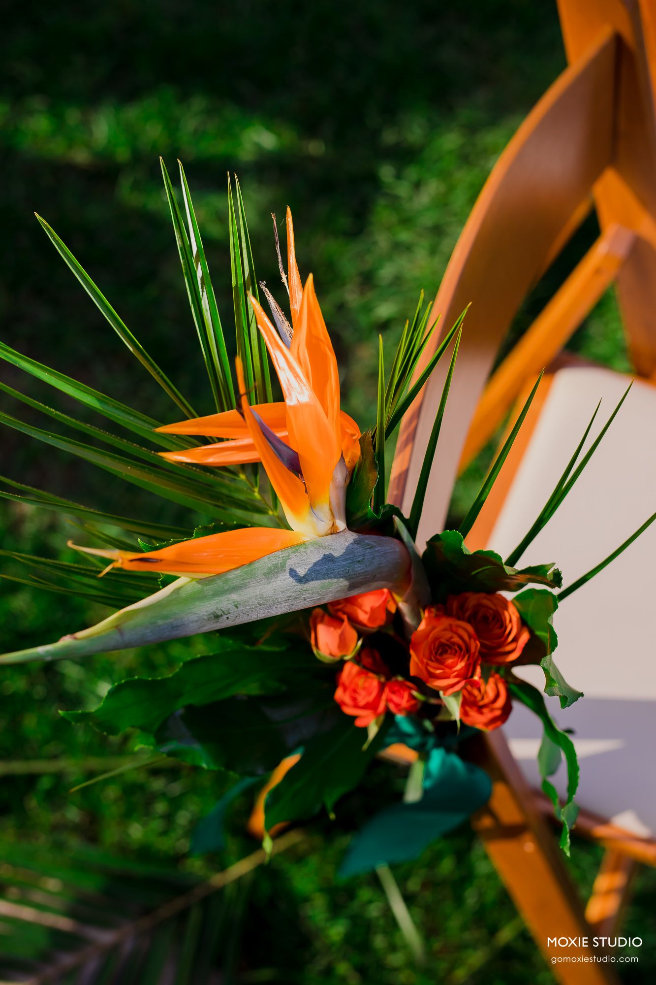 Tropical wedding arch decoration featuring orange bird of paradise flowers and red roses with green palm fronds.