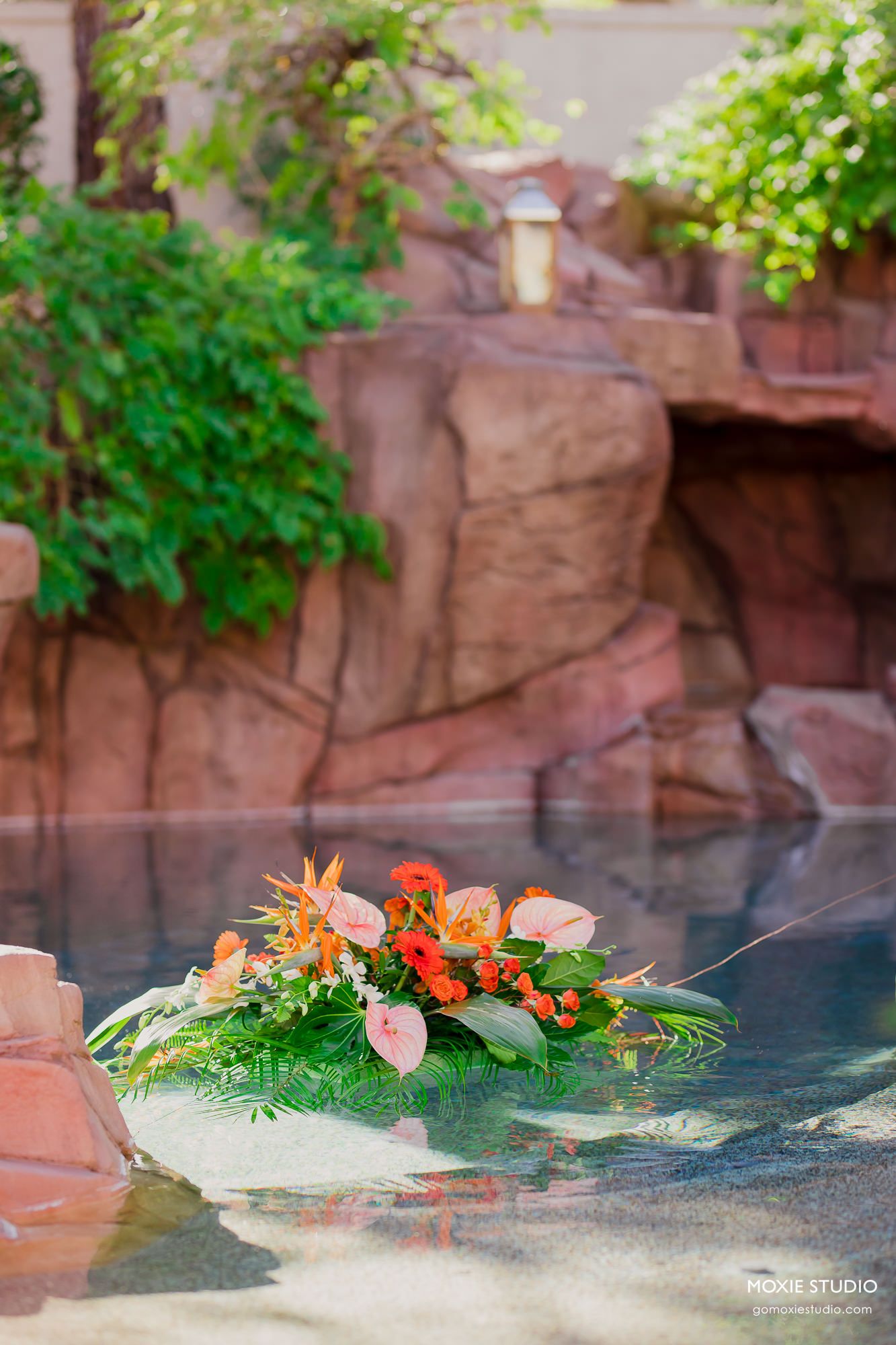 A floral arrangement with orange flowers and greenery floats gracefully on the surface of a tranquil pool of water.