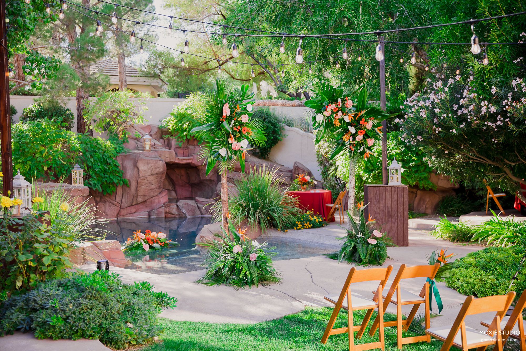 A curved garden pathway lined with lush greenery and orange wooden chairs leads through a peaceful outdoor setting.