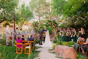 Wedding guests gather in a lush garden setting with wooden chairs arranged for an outdoor ceremony.