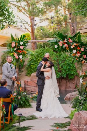 Wedding ceremony in a lush garden setting with tropical foliage and pink floral arrangements.