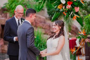A romantic outdoor wedding ceremony takes place in a lush garden setting with tropical flowers and greenery.