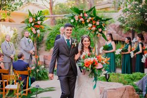 Wedding ceremony guests gather in a lush garden courtyard with blooming trees and string lights overhead.
