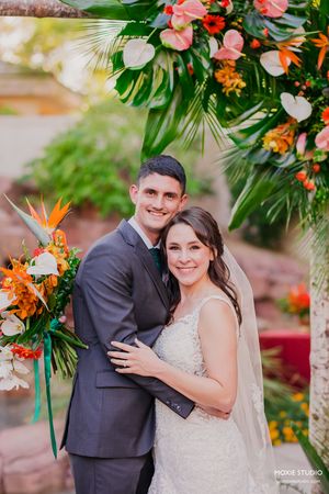 Romantic wedding couple poses together under tropical floral arrangements with orange and pink blooms.