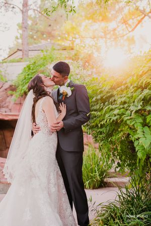 A romantic wedding couple embraces in a lush garden setting with golden sunlight filtering through the foliage.