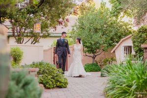 A couple walks along a scenic garden pathway lined with lush greenery and blooming flowers during a wedding celebration.