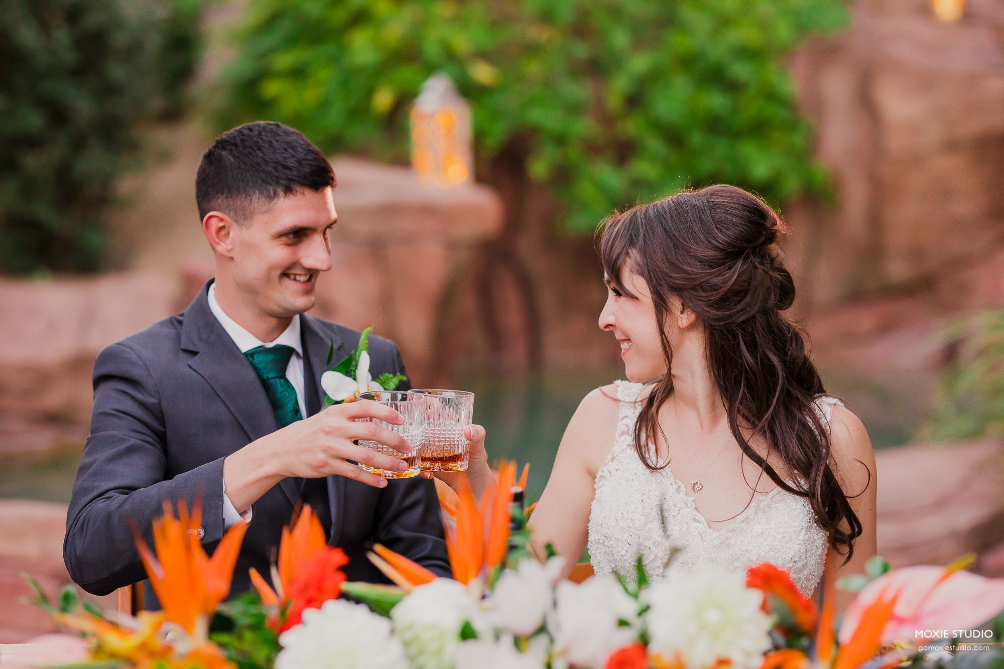 A couple shares an intimate moment at an outdoor wedding reception with vibrant orange floral centerpieces.