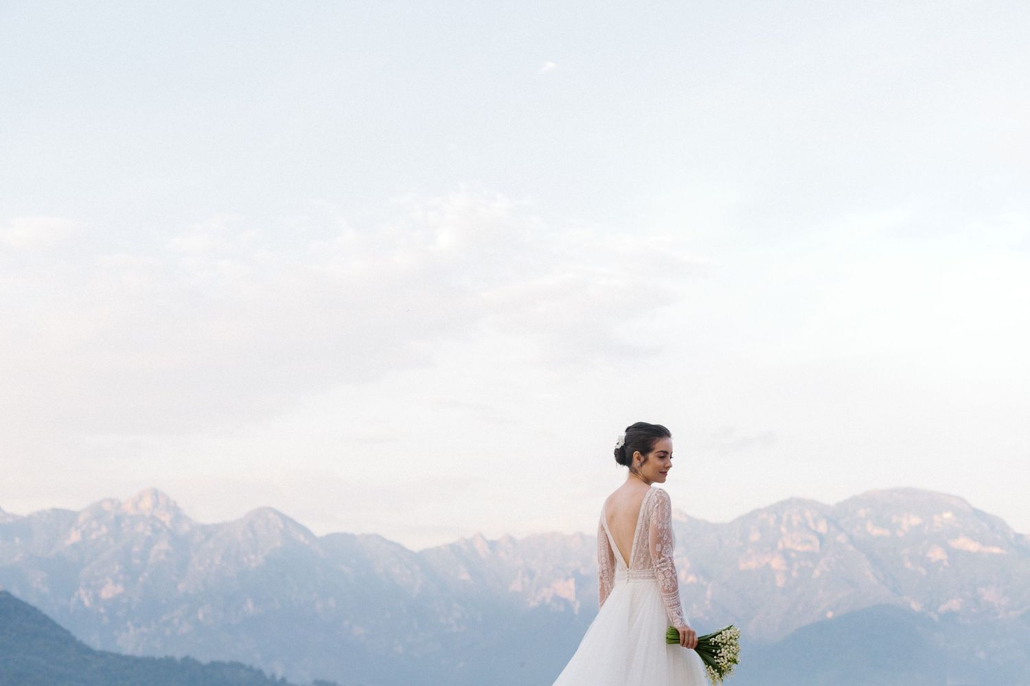 A bride in a white dress holds a bouquet while standing against a backdrop of majestic mountain peaks.