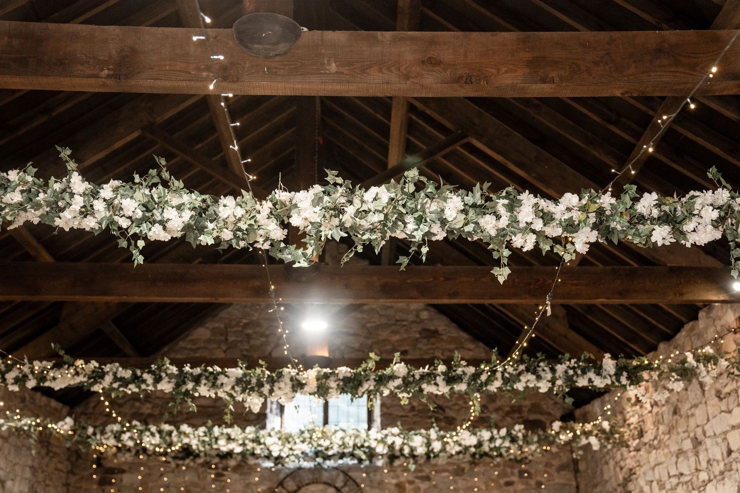 Rustic wooden beams and delicate white floral garlands create an enchanting wedding venue ceiling decoration.