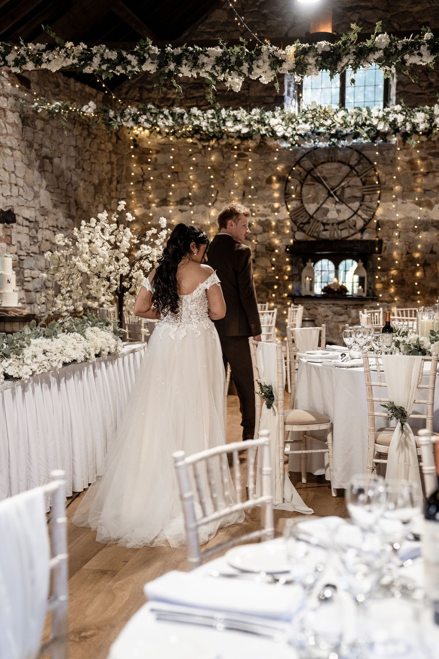 Elegant rustic barn wedding venue decorated with white flowers, fairy lights and stone walls creating romantic ambiance.