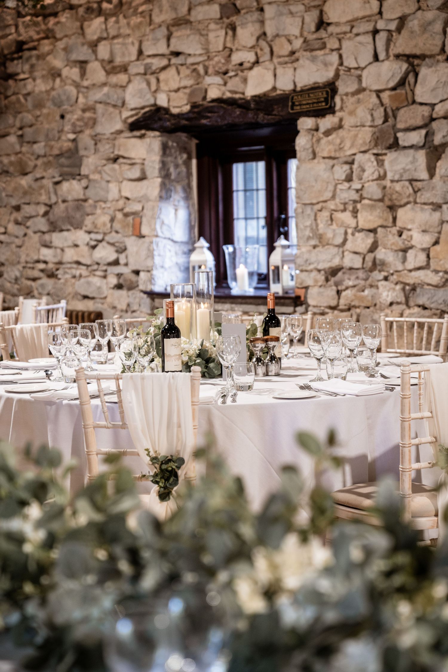Elegant wedding reception table setting with white linens and rustic stone walls in a romantic venue interior.