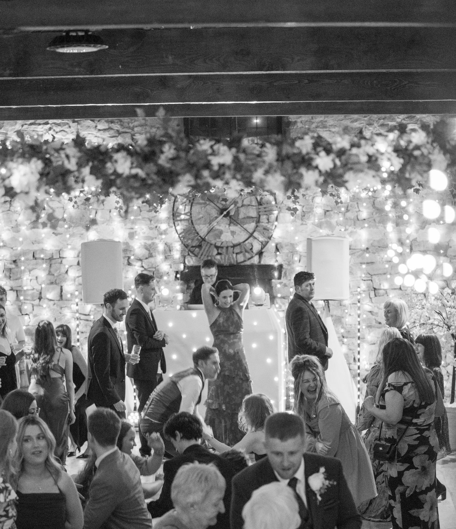 Wedding guests mingle and dance on a decorated dance floor during an evening reception celebration.