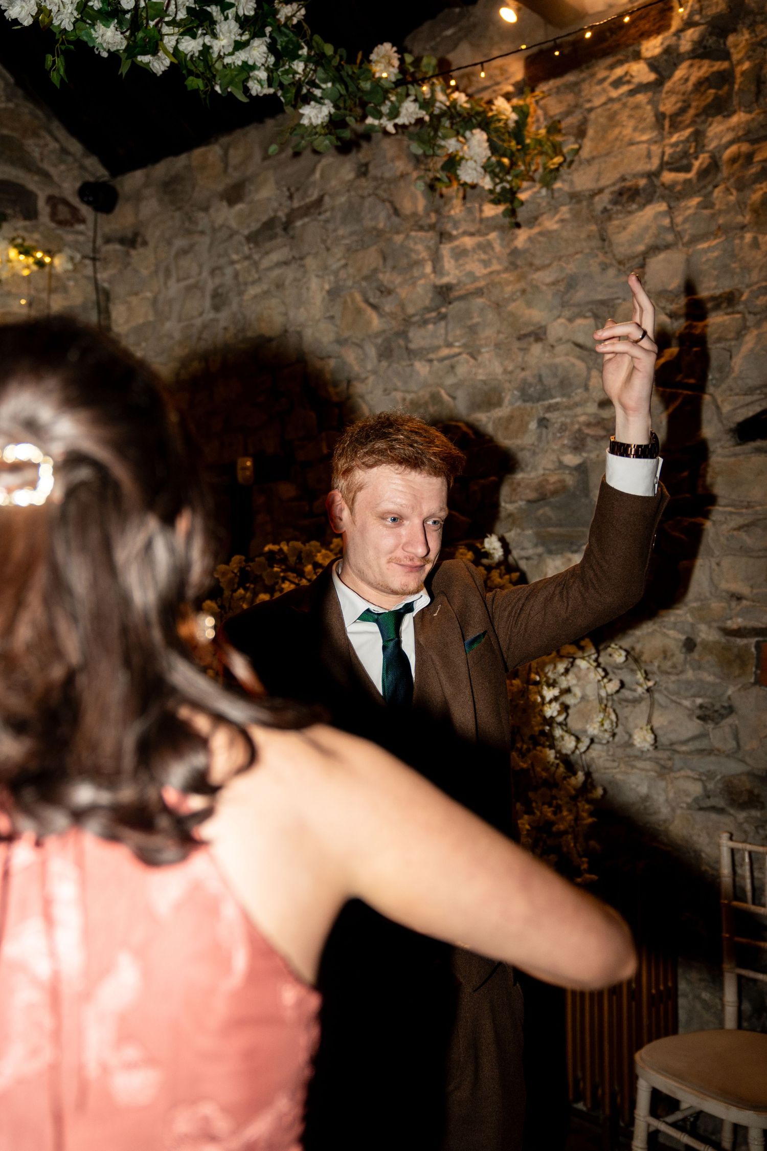 Guests dancing and celebrating at a rustic stone-walled venue illuminated by warm lighting.