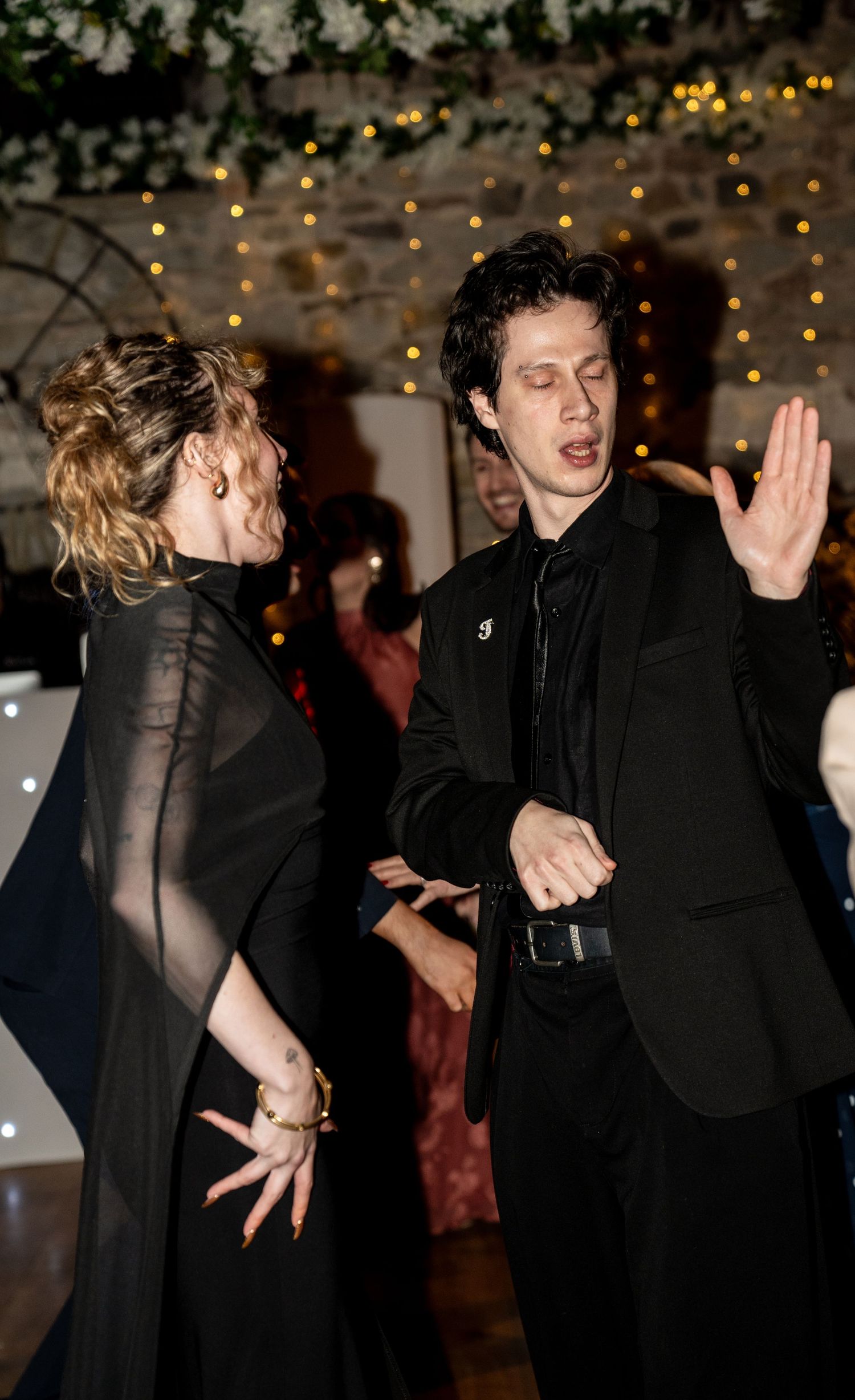 People dancing energetically at a party with twinkle lights in the background.