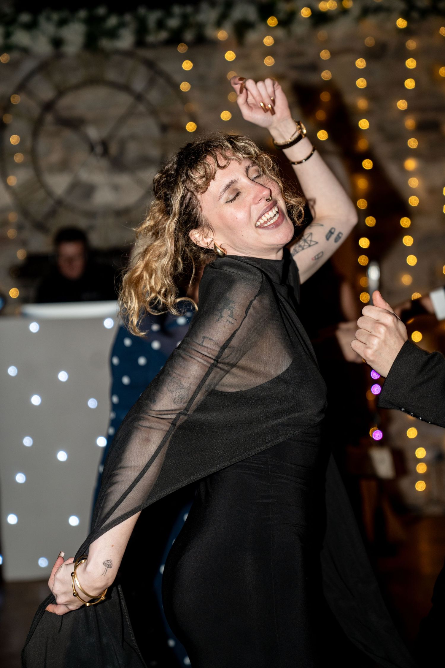 A joyful dancer in a black sheer dress twirls on the dance floor with string lights glowing in the background.