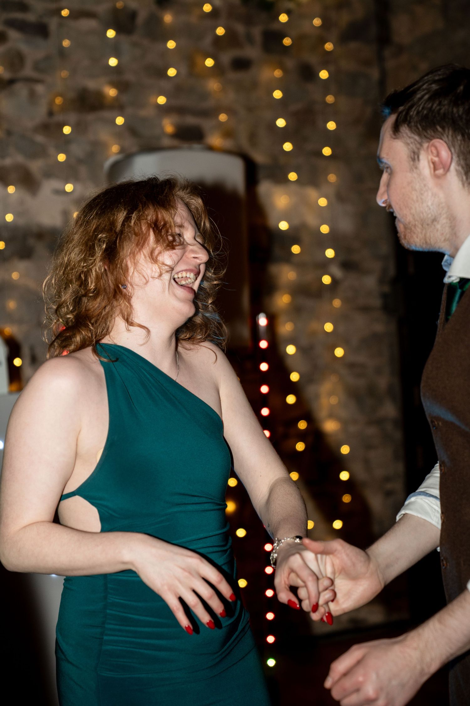 Two people share a lively dance moment against a backdrop of twinkling holiday lights at an indoor celebration.