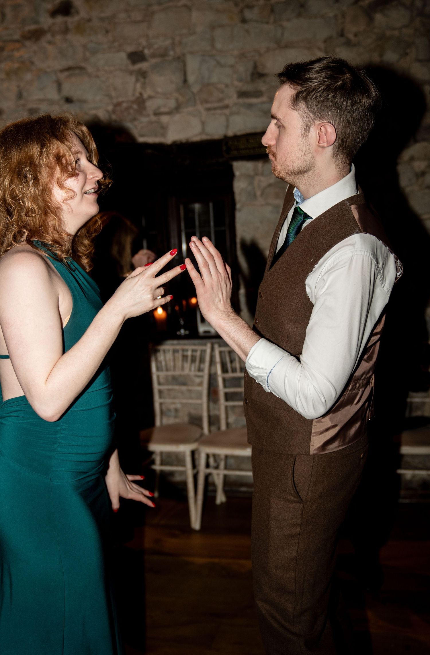 A couple dances together in a rustic brick venue, with the woman wearing a teal dress and man in brown vest.