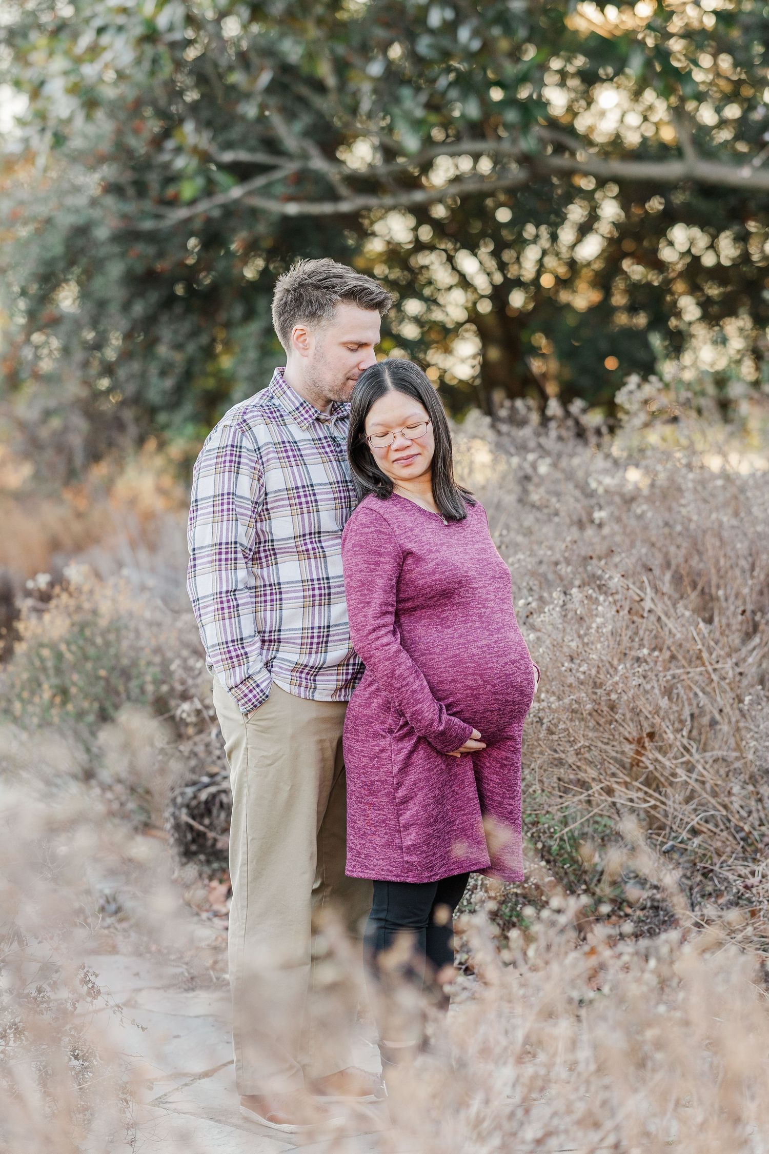 A couple shares a tender moment together in a field of dried grass during golden hour.
