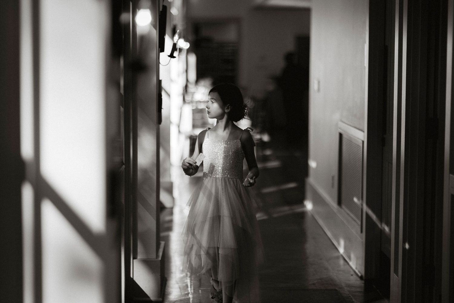 A dramatic black and white photo of a dark hallway with sunlight casting shadows through windows along the corridor.