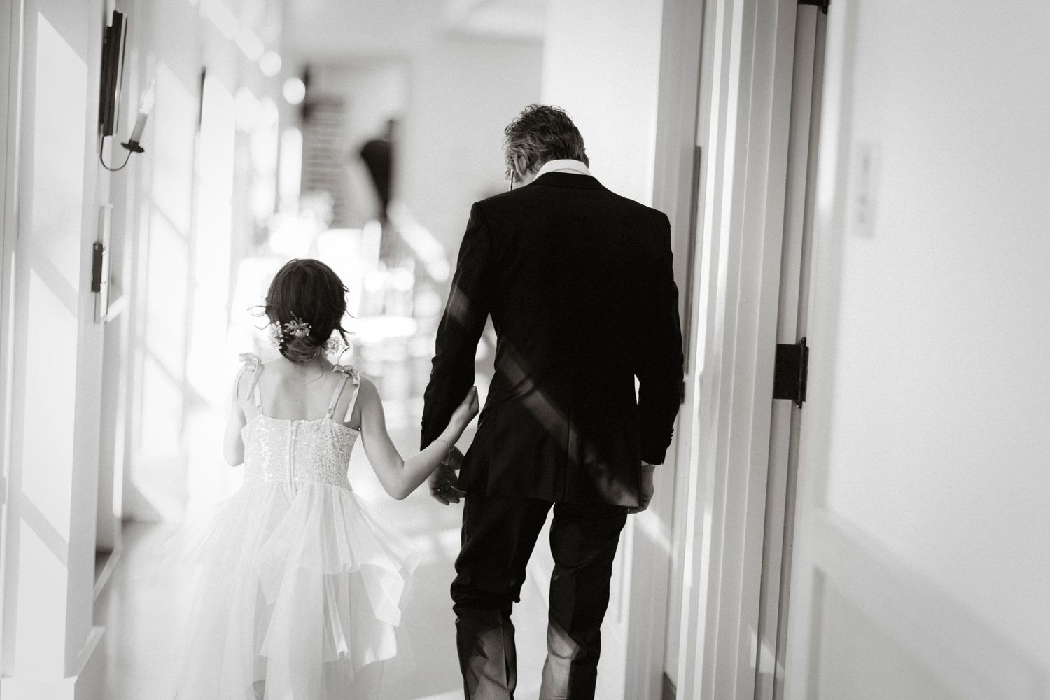 A bride and groom walk down a bright white hallway together after their wedding ceremony.