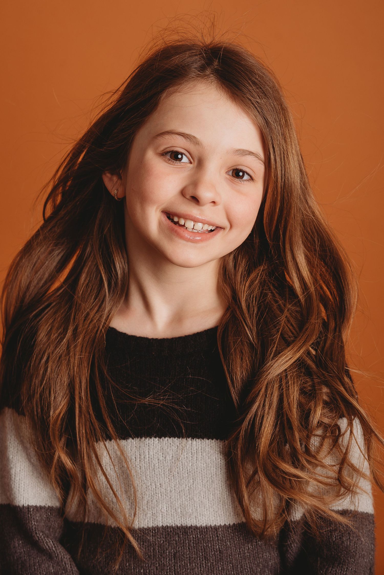 Close-up portrait in striped sweater with natural hair against orange background.